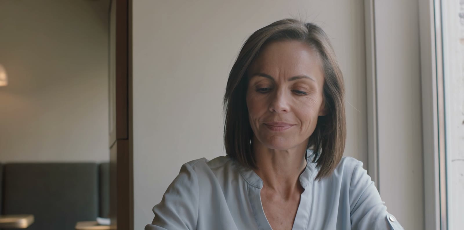 A woman at her laptop by a window, smiling calmly