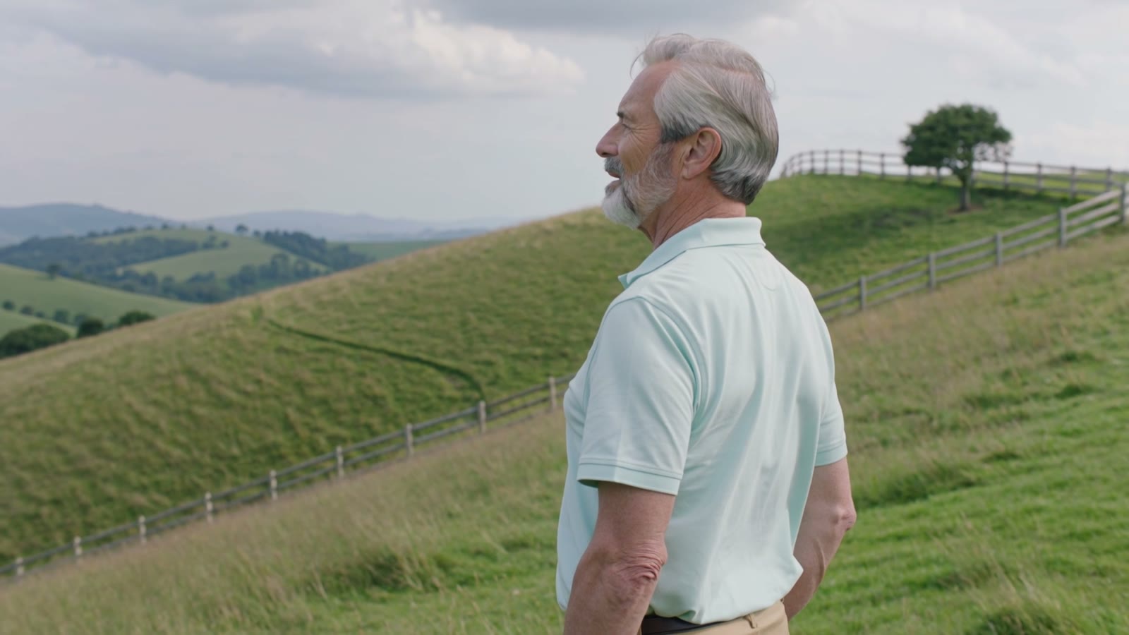 A man standing on a green hillside, gazing calmly into the distance