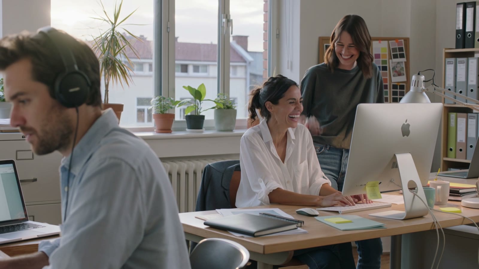 Two colleagues at a desk, smiling at something on the screen together